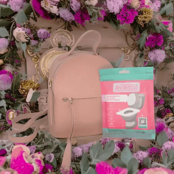 Sobre de saniasientos Twaletta junto a una mochila pequeña entre flores
